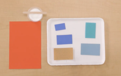orange paper with white tray with strips of paper and a container of glue above on a table